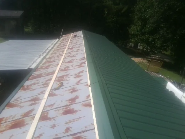 Old rusted panels beside newly installed green metal roofing — Wind Damage Roof Repair by Roofing Brothers in Barnesville