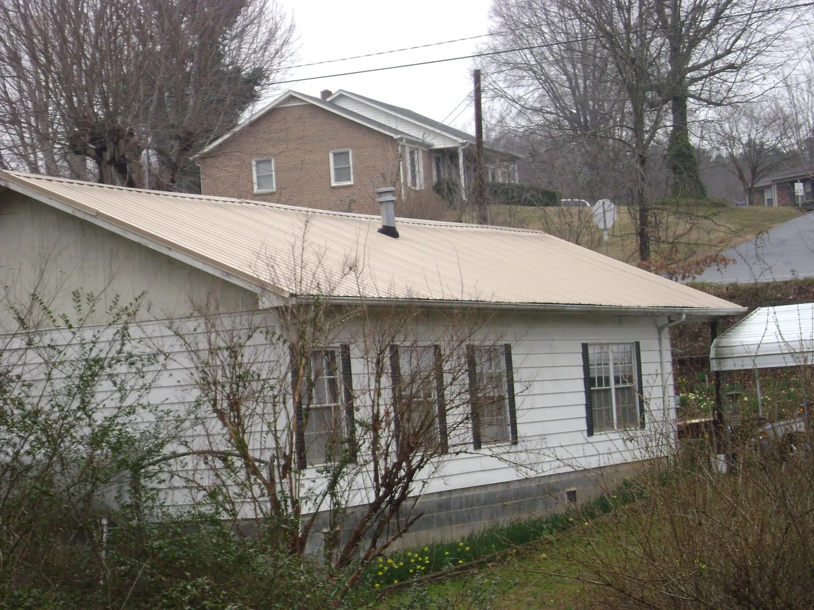 Tan metal roof on a white sided house set into a hillside — Commercial Roofing by Roofing Brothers in Barnesville