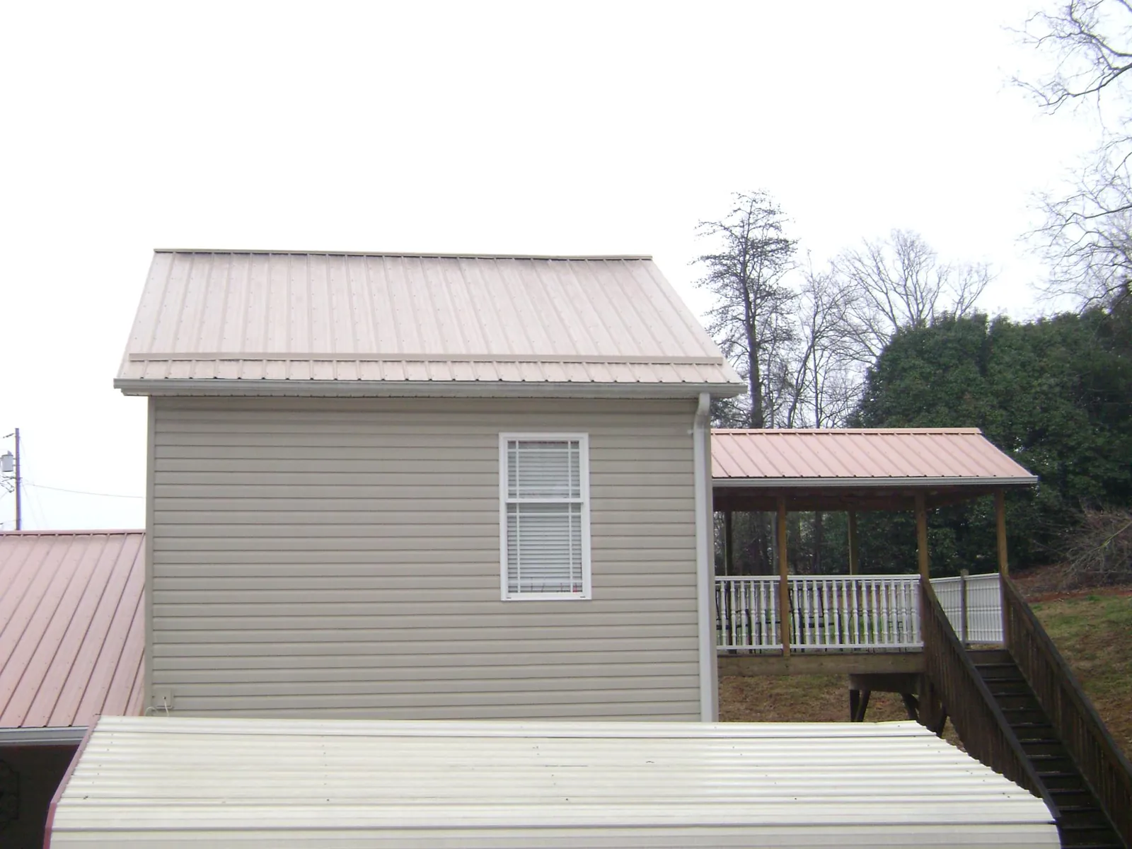 Tan metal roofs on a two story addition and attached porch, from a Roof Replacement job in Barnesville